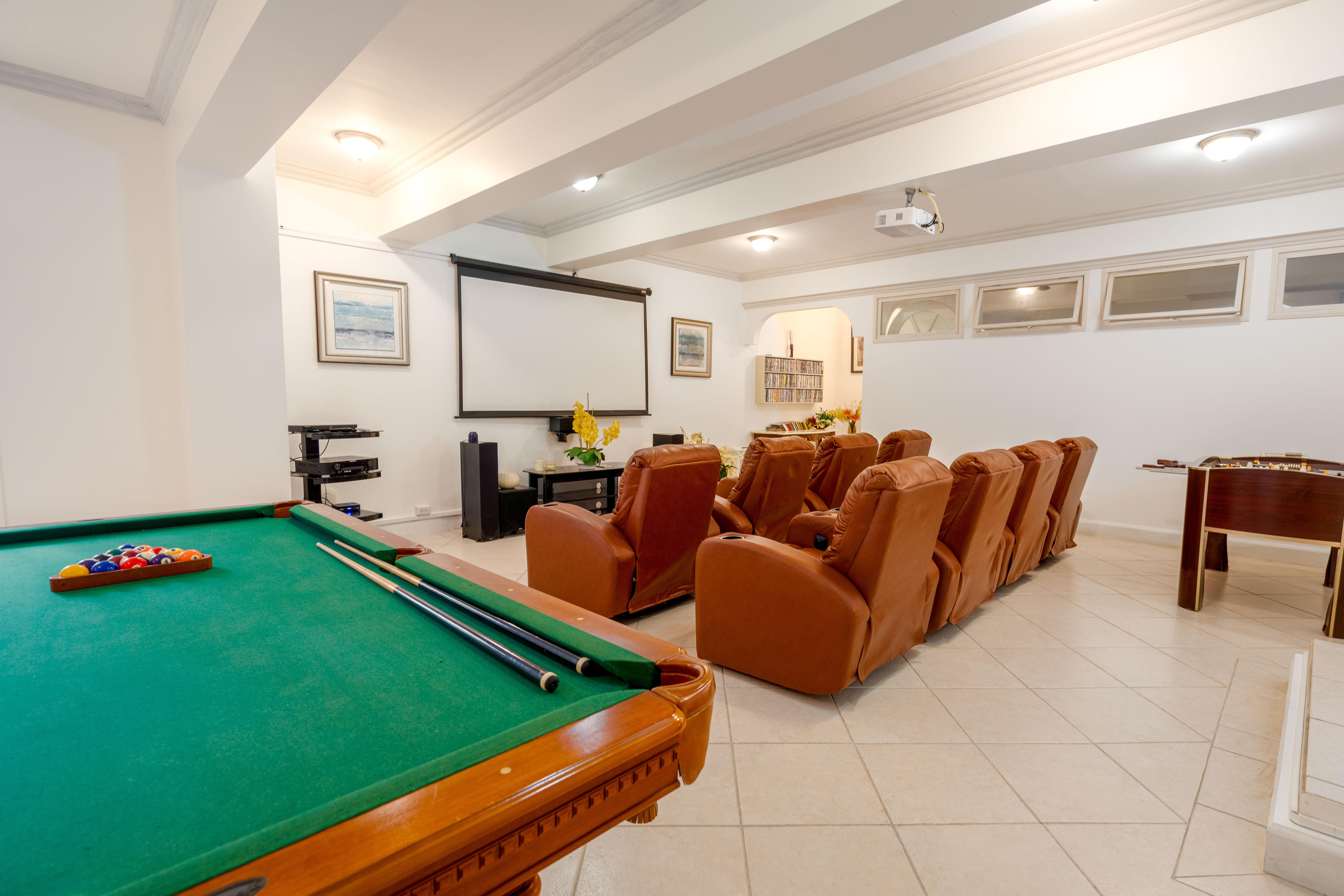 Home cinema with eight leather armchairs in front of a large projector screen, with a pool table to one side