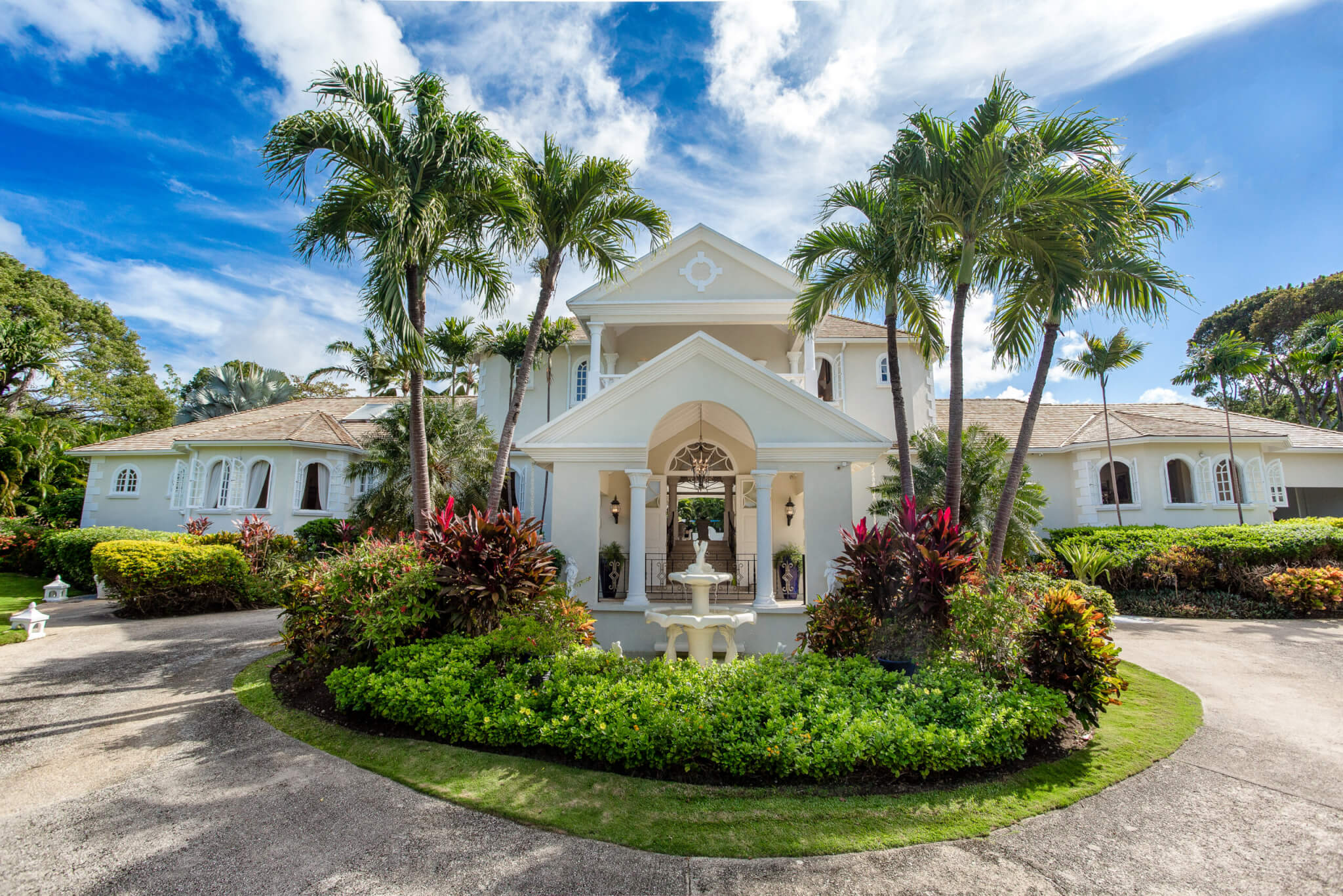 Entrance to a very large luxurious white house with palm trees