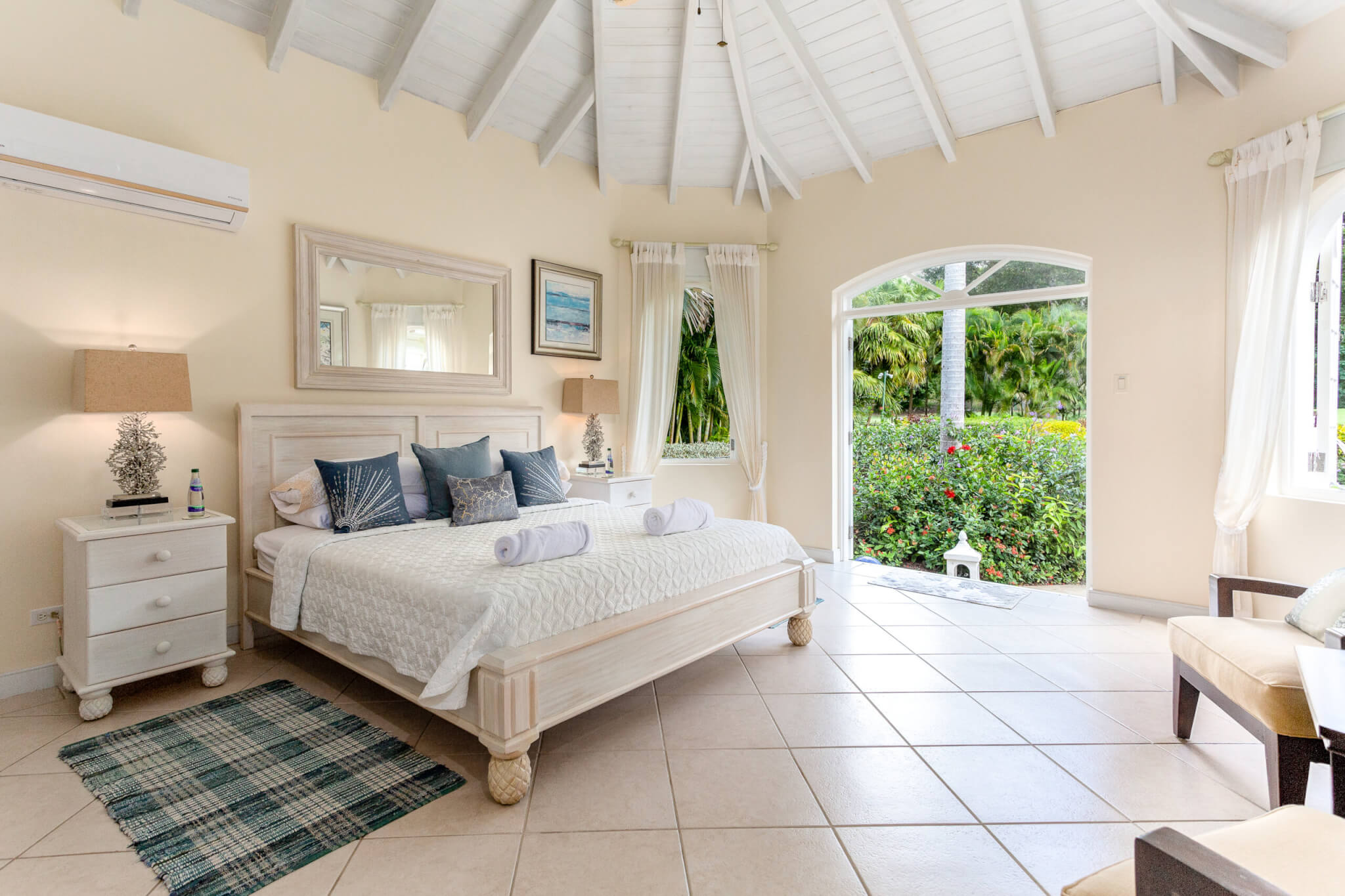 Bedroom with a king size bed, two white bedside tables with lamps, high ceiling and direct access to the garden