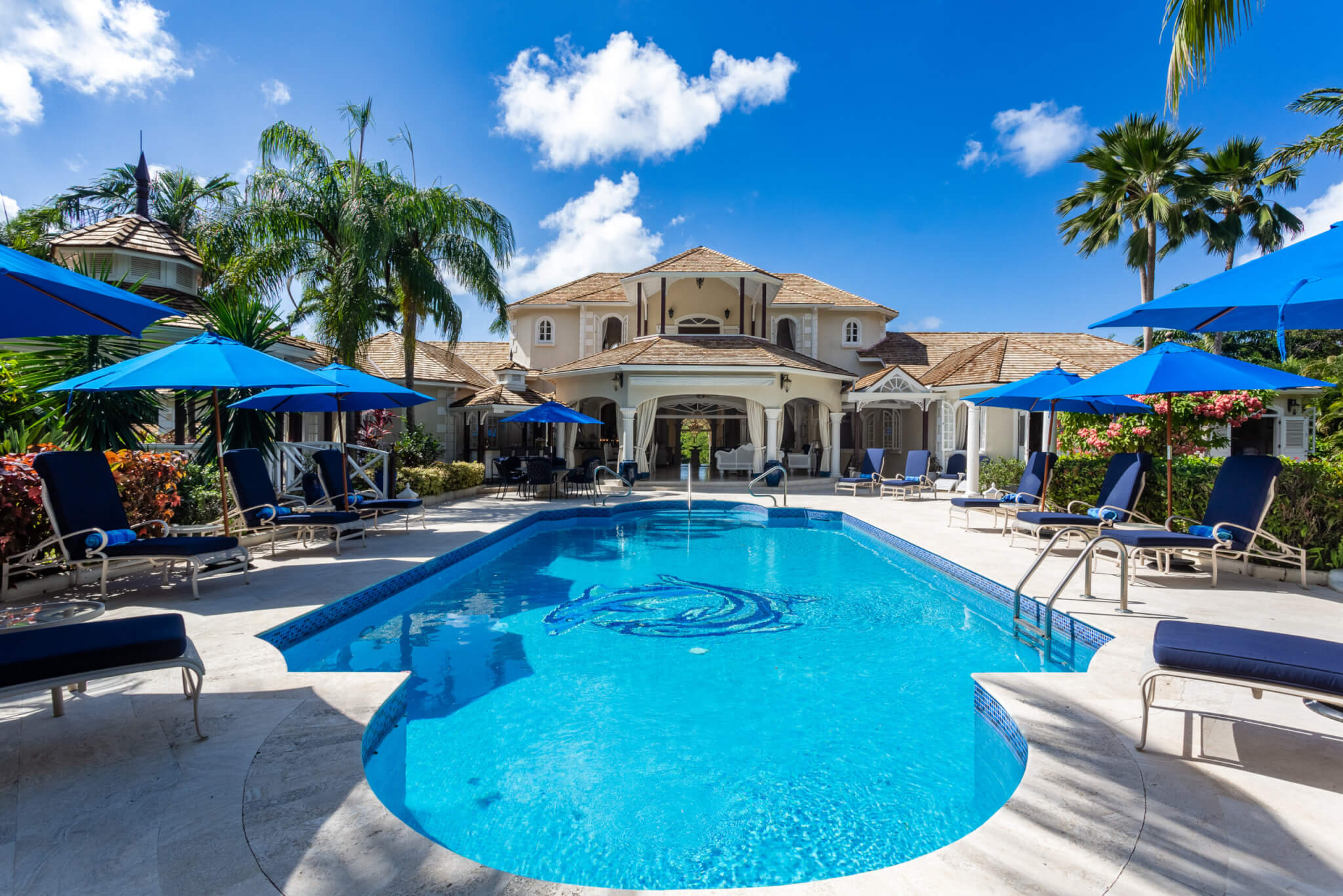 Large pool with a large house in the background with blue skies above